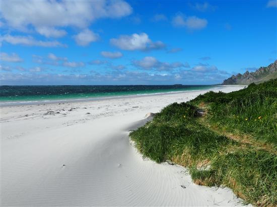 Bilde av Bleiksstranda, med sand, en gressbank og bleiksfjellene i horisonten.  - Klikk for stort bilde